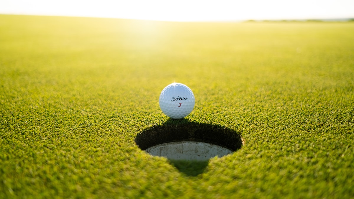 Golf ball resting on the lip of the cup on a sunlit green